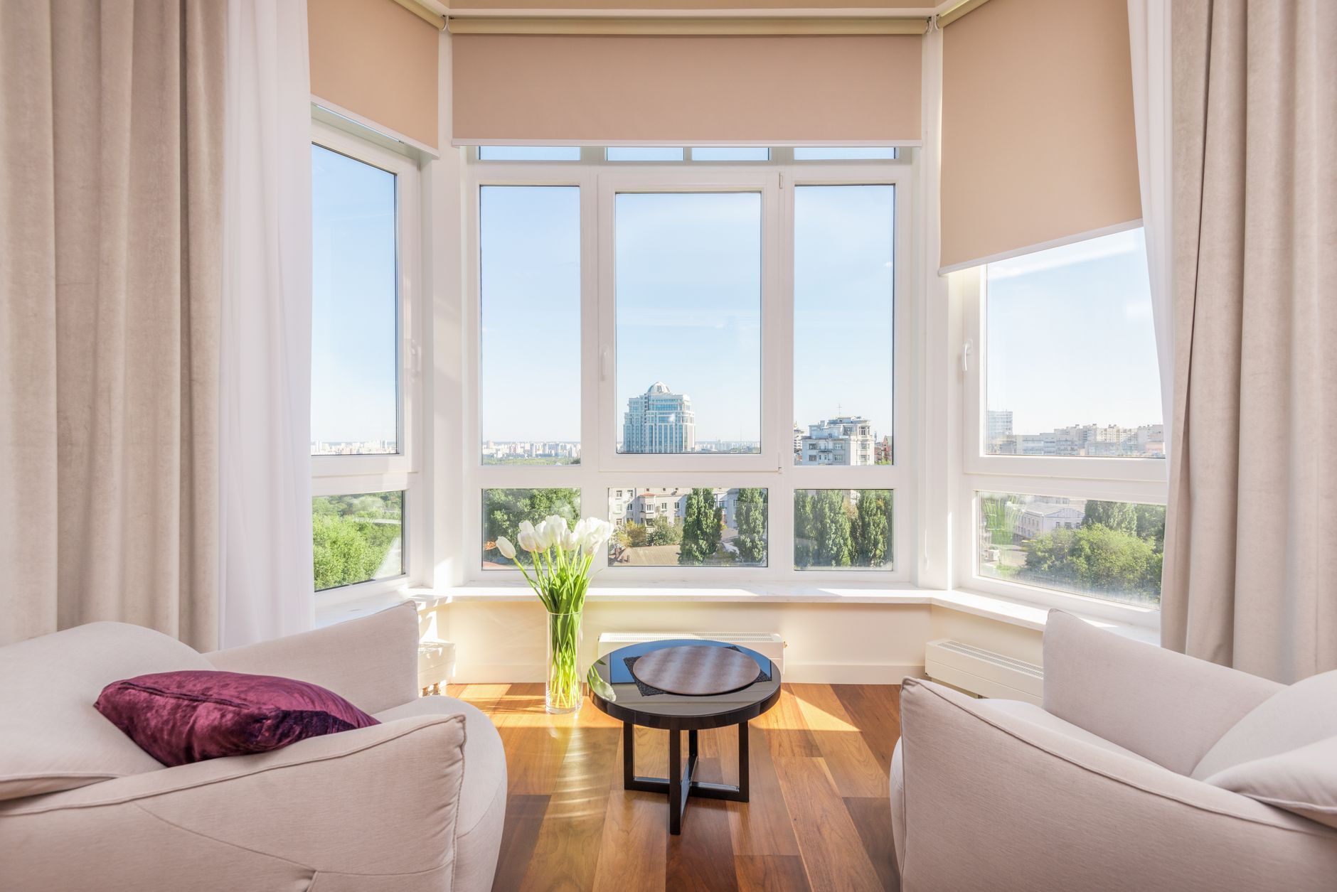 Salón luminoso con grandes ventanas de PVC, sillones claros y suelo de madera bañado por la luz del sol